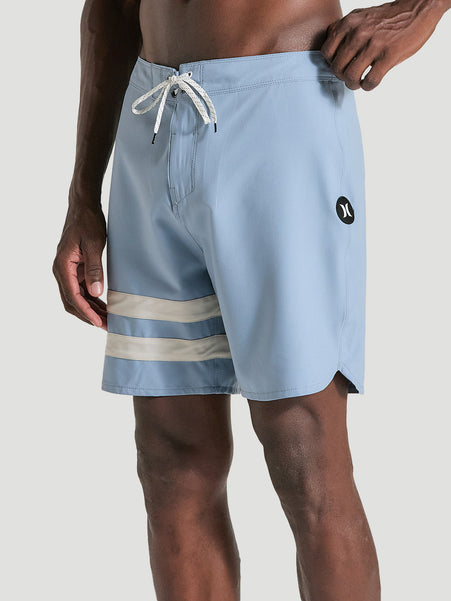 Homem vestindo boardshorts phantom 18 polegadas azul, com listras brancas na perna esquerda. Cordão ajustável na cintura e logo preto na lateral.