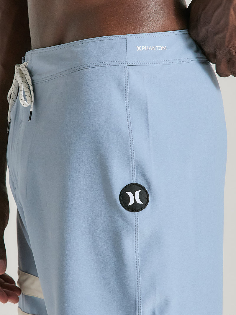 Close do boardshorts phantom 18 polegadas azul, com cordão branco ajustável, logo preto circular na lateral e costura detalhada.