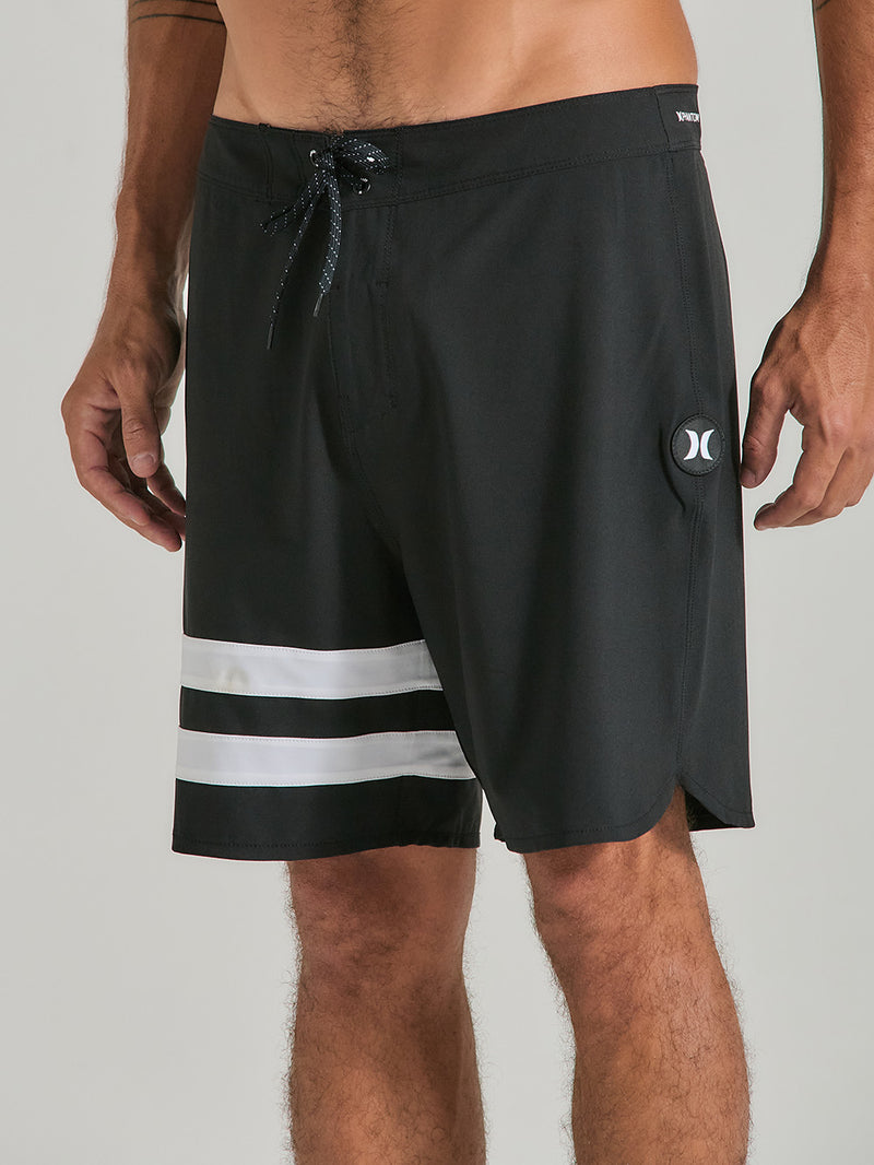Homem vestindo o boardshorts phantom 18 polegadas preto, com detalhe de listras brancas na perna esquerda e logo discreto. Modelo esportivo.