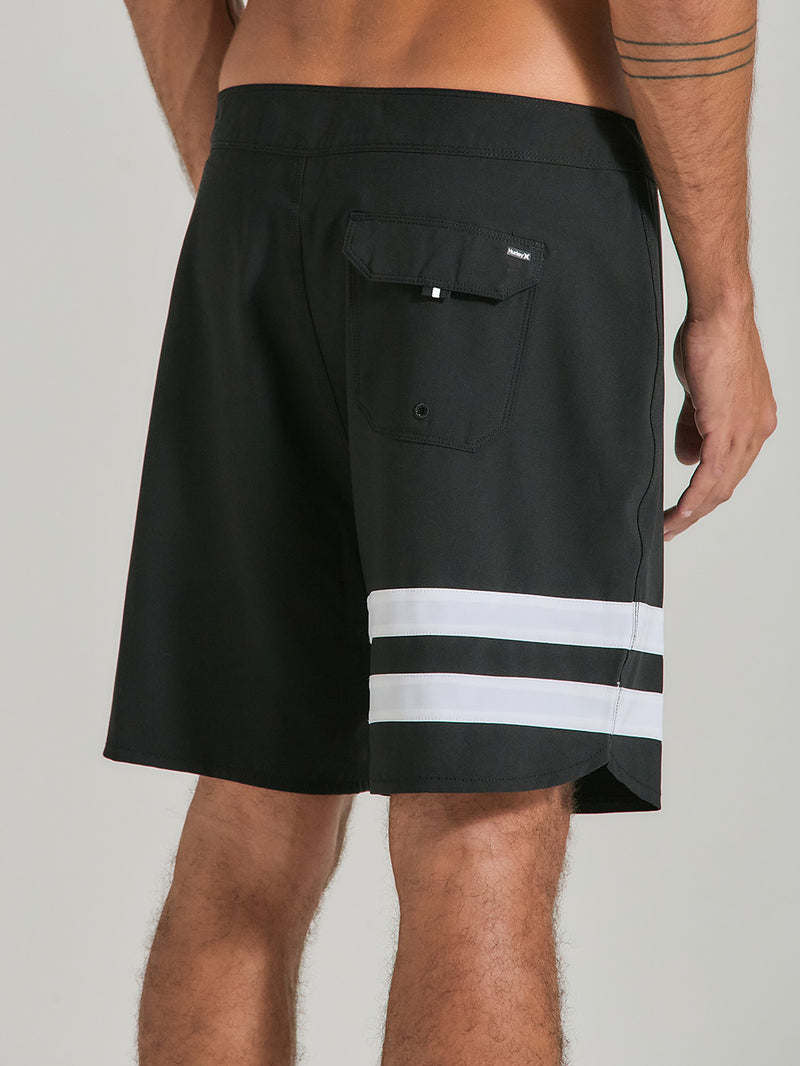 Homem de costas vestindo boardshort phantom 18 polegadas preto, com listras brancas na perna esquerda e bolso traseiro com aba. Estilo esportivo.