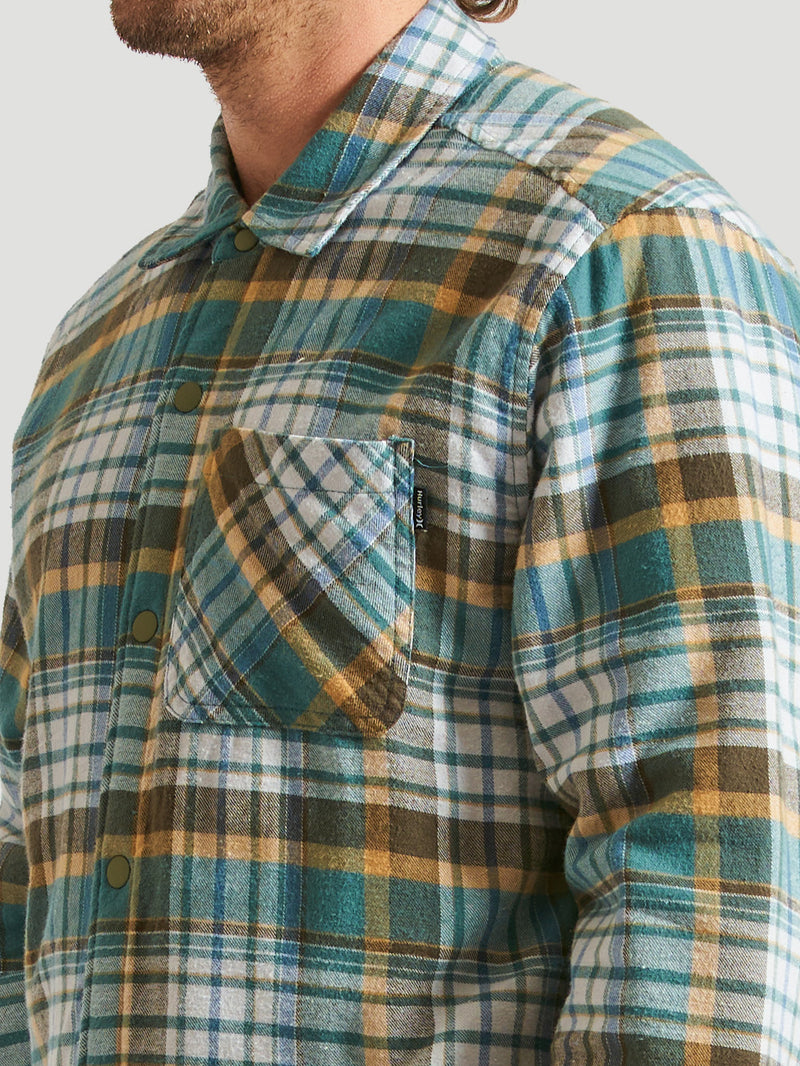 Camisa de flanela xadrez em tons de verde, branco e amarelo, com bolso frontal no peito, fechamento por botões e tecido macio.