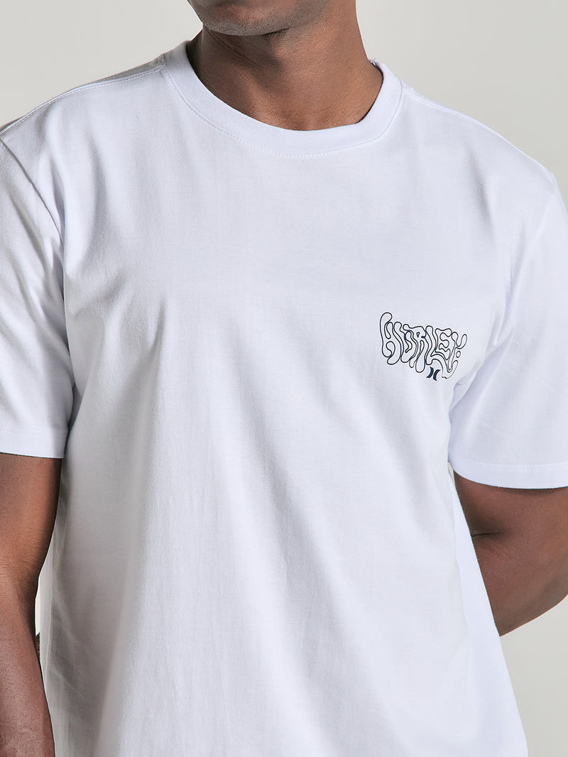 A imagem mostra uma camiseta branca manga curta estampa relevo, com um estilo minimalista e uma estampa localizada no lado esquerdo do peito. A estampa utiliza linhas estilizadas, criando um efeito visual interessante e moderno.