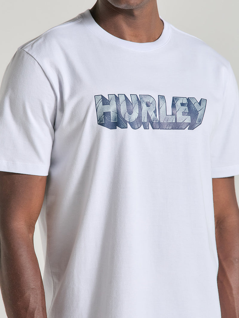 Close da camiseta branca manga curta estampada com gola redonda. A estampa destaca Hurley em fonte azul com efeito 3D texturizado.
