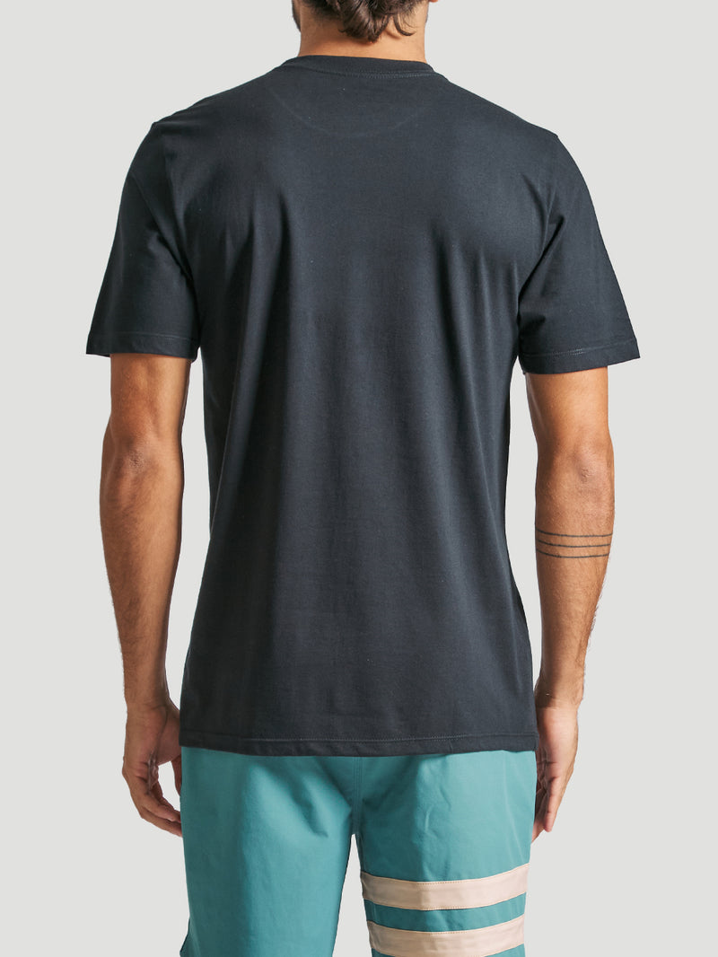 Homem de costas veste camiseta em algodão preta de tecido liso, manga curta, com caimento reto, combinada com bermuda azul com detalhes em branco e bege.