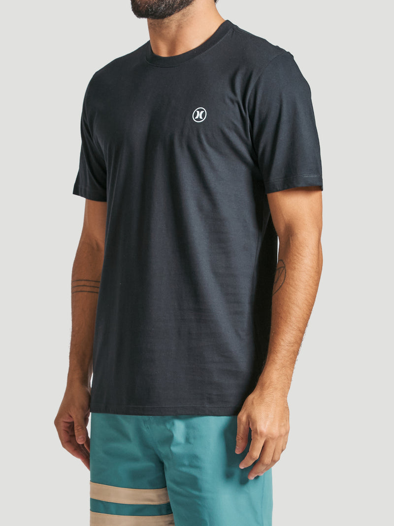 Camiseta em algodão preta com gola redonda, manga curta, tecido liso e pequeno logo branco no peito, combinada com bermuda azul com detalhes bege.
