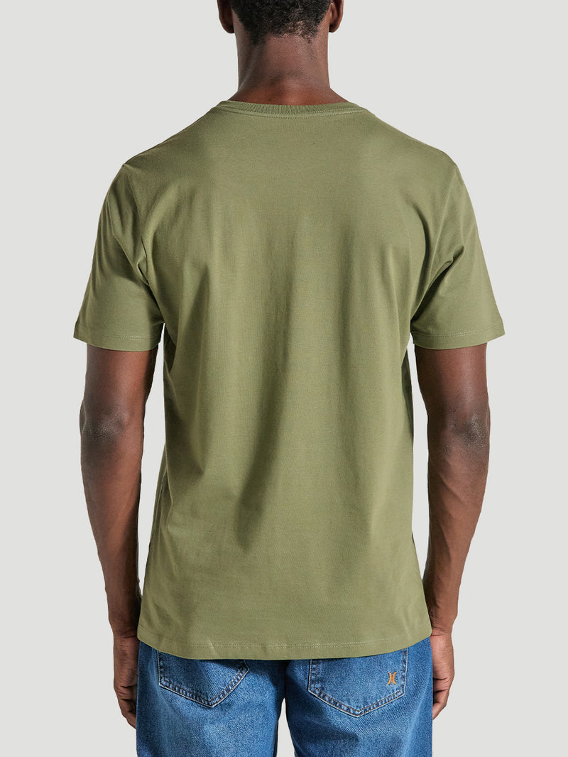 Homem de costas usando camiseta em algodão verde militar com corte básico, gola redonda e mangas curtas, combinada com calça jeans azul.
