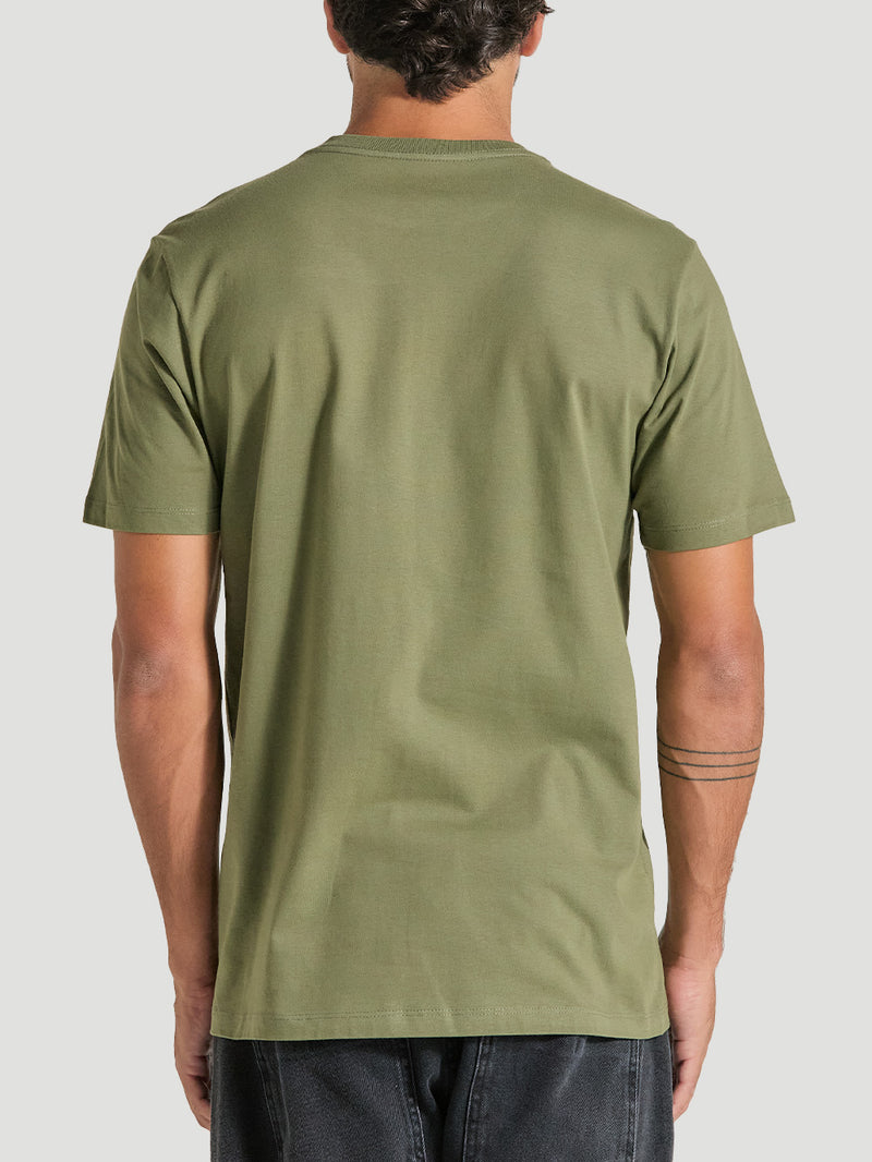 Homem de costas veste uma camiseta verde manga curta de tecido liso, caimento reto, combinada com calça preta, em fundo neutro cinza claro.