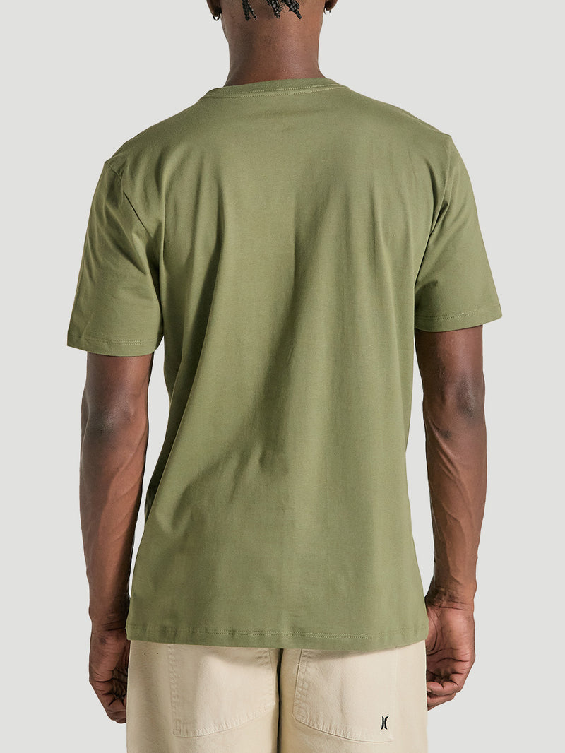 Homem vestindo a camiseta verde militar estampa frontal manga curta vista por trás, combinada com uma bermuda bege, sobre fundo neutro.