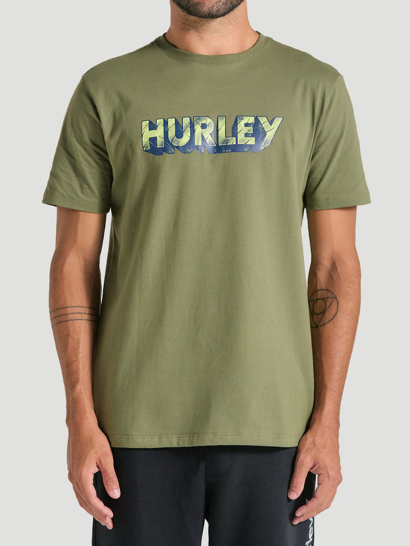 Homem vestindo camiseta verde militar estampada com logotipo "Hurley" em tons de azul e amarelo.