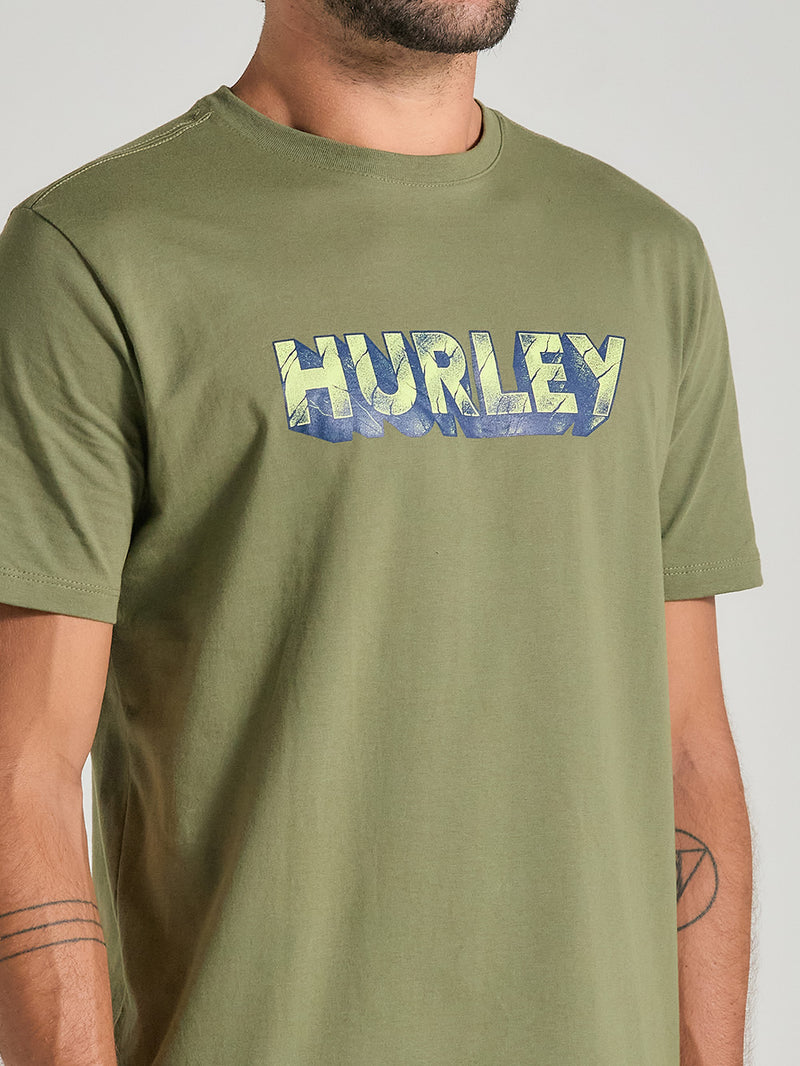 Camiseta verde militar estampada com o logotipo "Hurley" em letras estilizadas com tons de azul e amarelo.