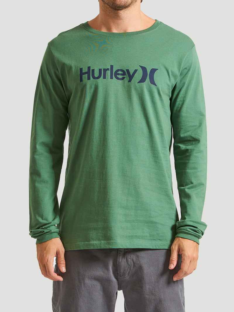 Camiseta verde militar manga longa com estampa do logo "Hurley" em azul escuro, combinada com calça cinza. Fundo cinza claro.