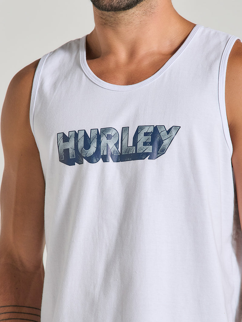 Homem usando regata branca estampada com o logo "Hurley" em azul metálico centralizado. A peça possui tecido leve, corte reto e alças largas.