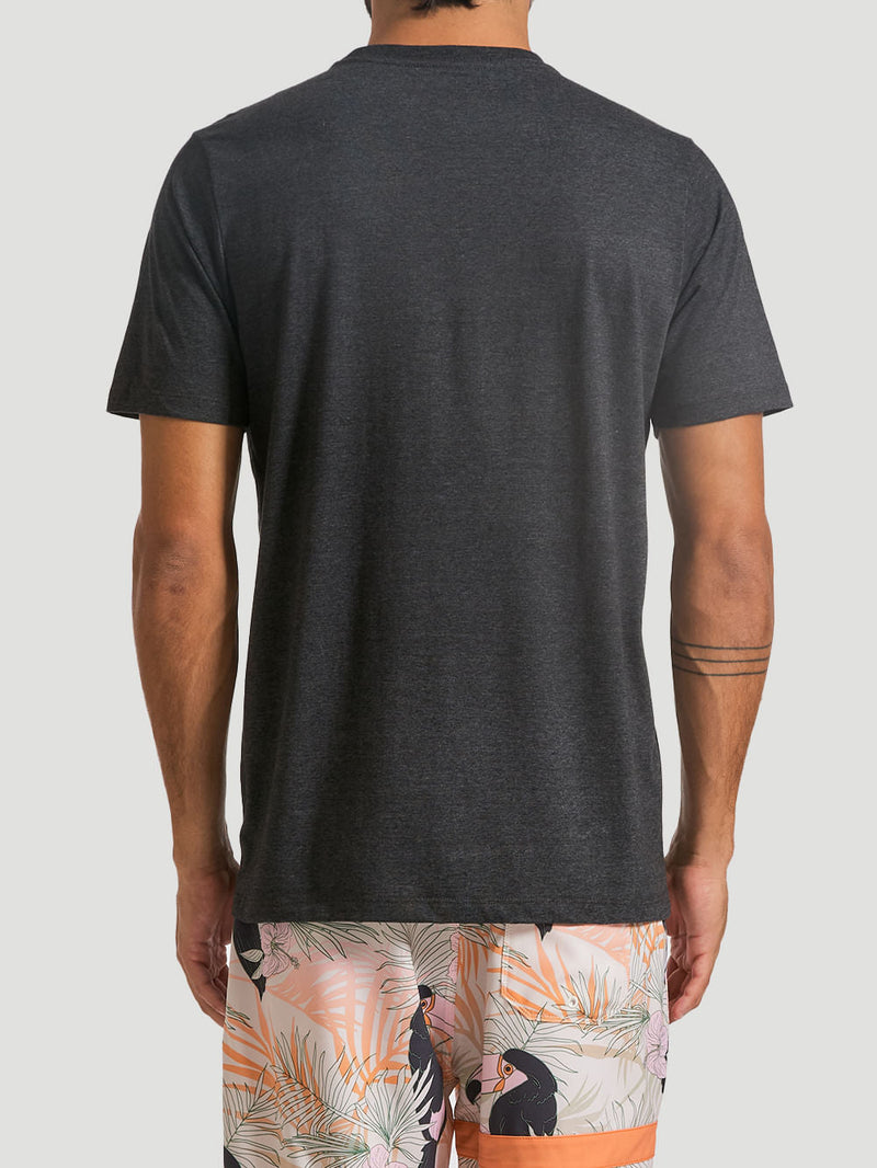 Homem veste uma camiseta estampada algodão preta, de manga curta e sem estampas na parte traseira, combinada com uma bermuda estampada com tucanos e folhas tropicais em tons pastel.