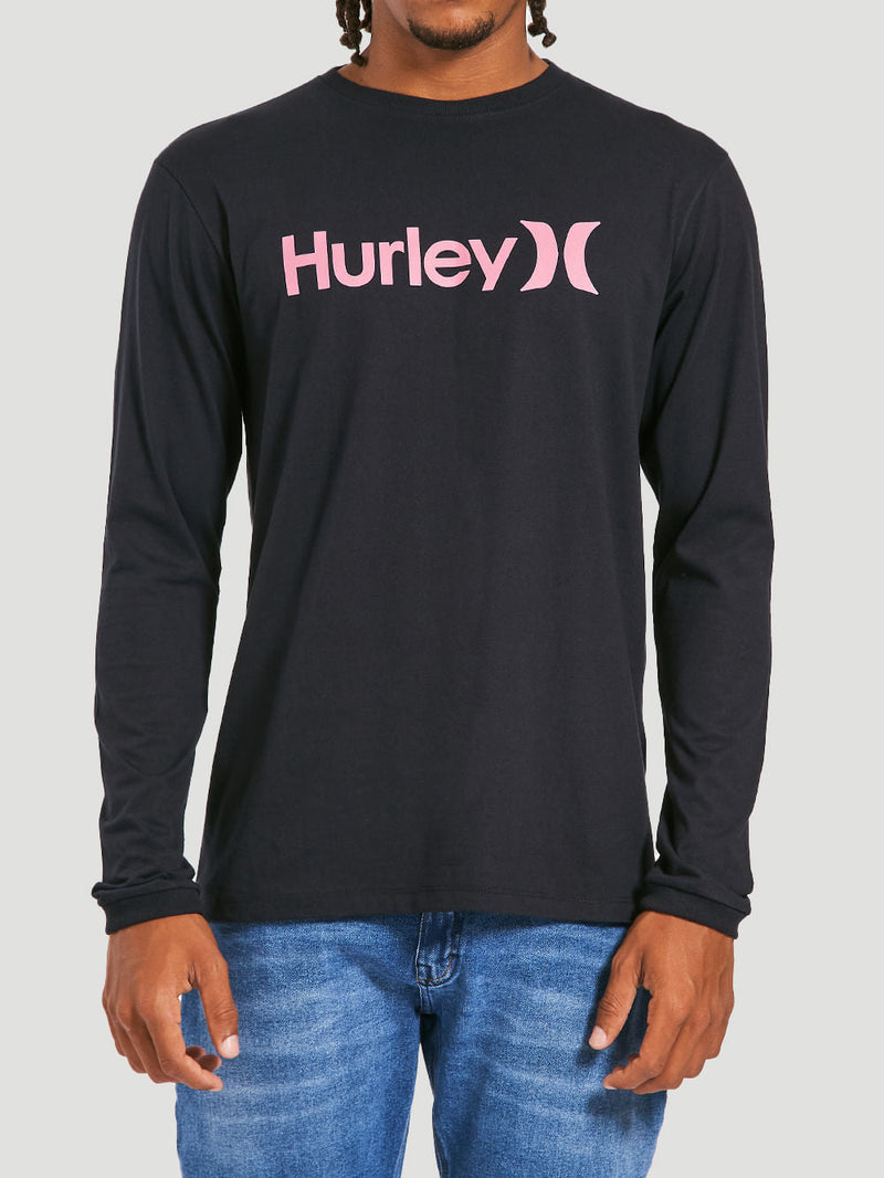 Homem vestindo uma camiseta preta manga longa com estampa frontal rosa com o texto "Hurley", combinada com calça jeans clara. Fundo cinza claro.