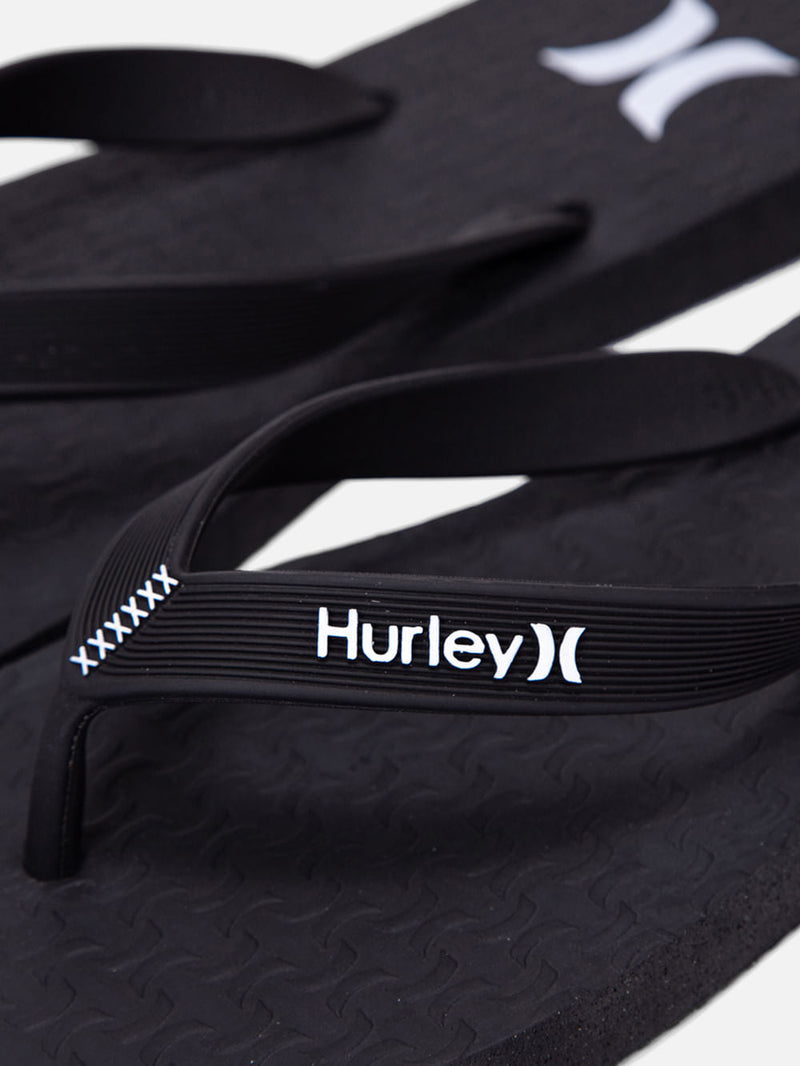 Chinelo Hurley preto com tiras emborrachadas, logotipo branco e detalhes texturizados no solado. Design casual e confortável.