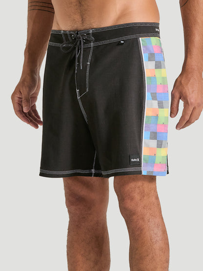 Homem vestindo boardshorts phantom 16 polegadas preto com detalhe lateral em estampa xadrez colorida. A bermuda possui cintura com amarração e costura em destaque.