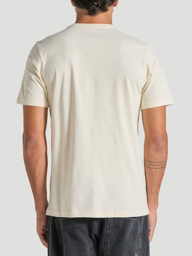 Homem de costas usando uma camiseta algodão básica off white com gola redonda e mangas curtas, combinada com calça jeans escura.