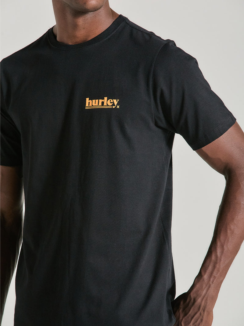 Camiseta algodão básica preta com gola redonda e mangas curtas. O design inclui o logotipo Hurley em amarelo no lado esquerdo do peito.
