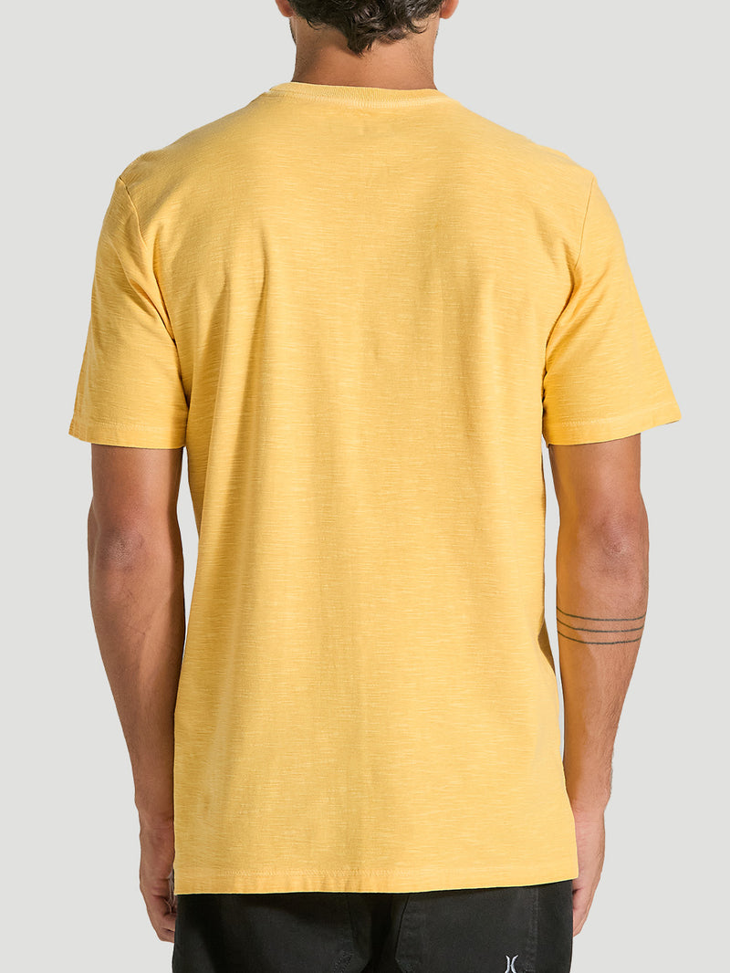 Camiseta amarela tinturada manga curta vista de costas, com textura suave no tecido, combinada com bermuda preta. Fundo cinza claro.