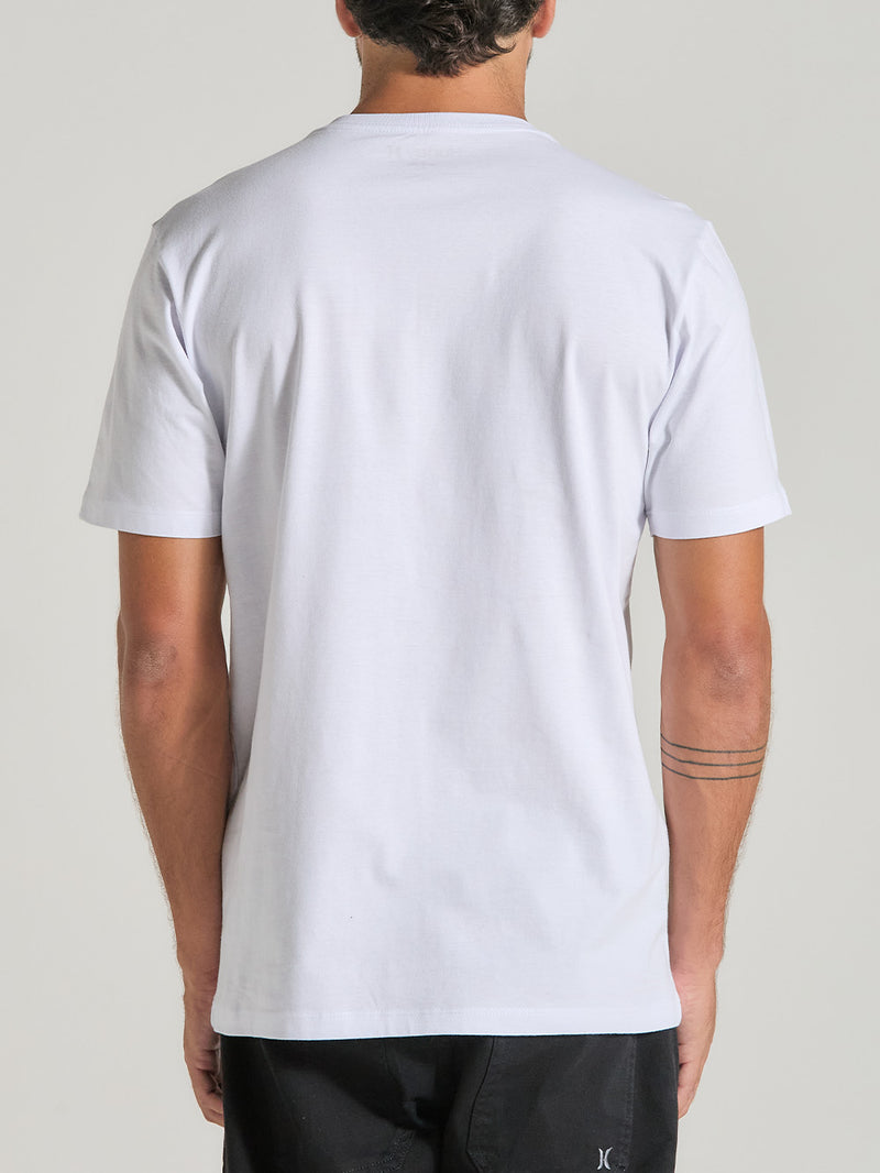 Homem de costas veste uma camiseta branca manga curta com tecido liso e caimento reto, combinada com calça preta, em fundo neutro.