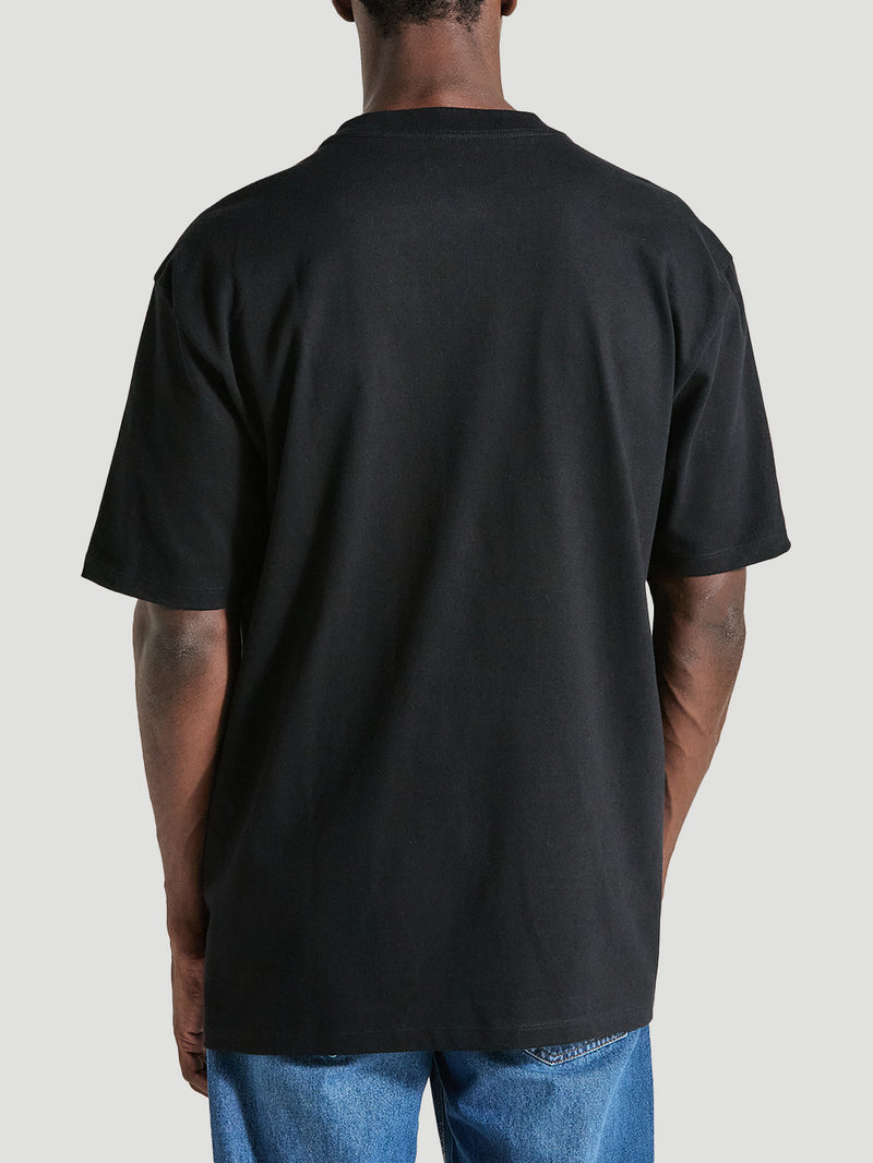 Homem de costas vestindo uma camiseta de algodão oversized preta manga curta, sem estampas visíveis, combinada com calça jeans azul clara.
