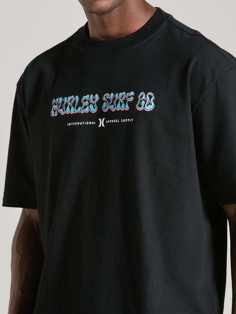 Homem usando a camiseta de algodão oversized preta manga curta com estampa "Hurley Surf Co." em fonte colorida, combinando estilo casual e moderno.