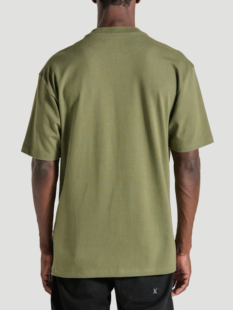 Homem de costas vestindo a camiseta de algodão oversized verde militar manga curta, sem estampas visíveis, combinada com bermuda preta casual.