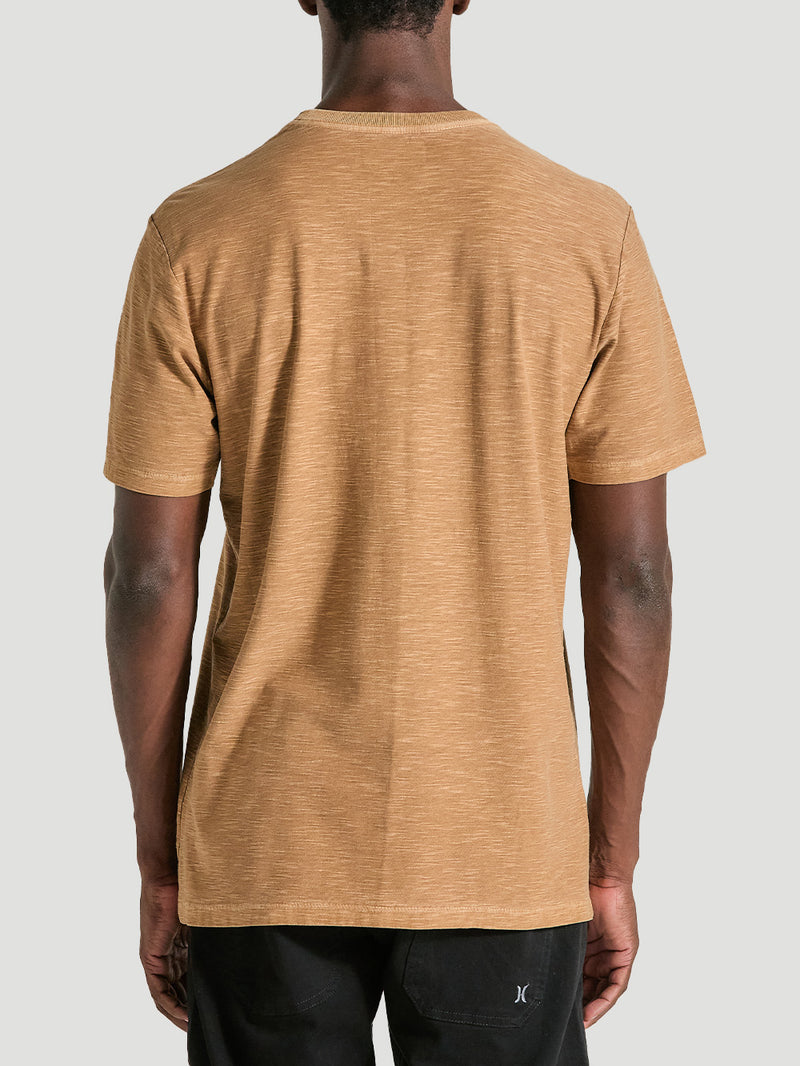 Camiseta marrom tinturada manga curta vista de costas, combinada com bermuda preta com logo discreto. Fundo neutro claro.