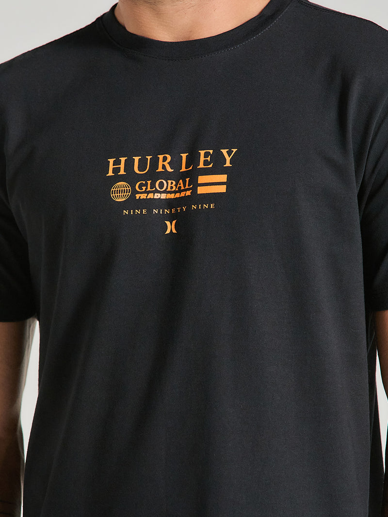Homem usa camiseta preta estampa frontal manga curta com escrita "Hurley Global Trademark" e elementos gráficos minimalistas.