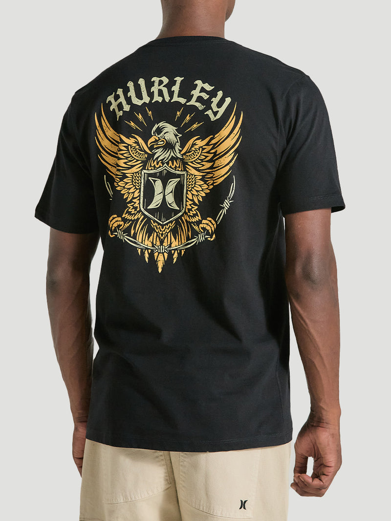 Homem vestindo camiseta preta manga curta estampa com grande desenho nas costas. A arte apresenta um escudo e uma águia dourada, junto ao logotipo "Hurley".