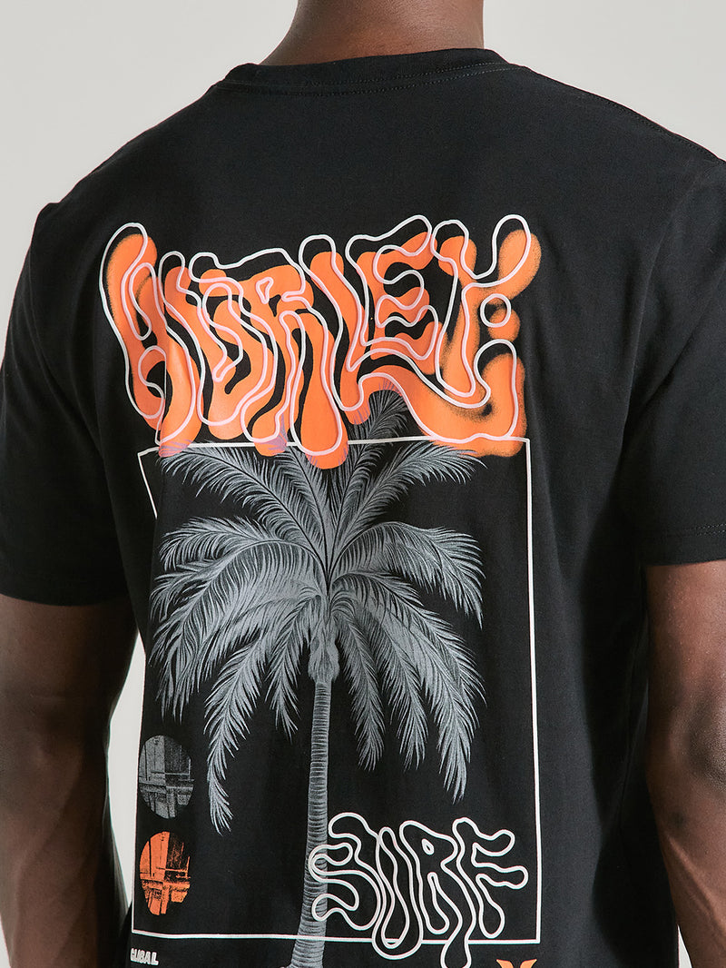 Camiseta preta manga curta estampa nas costas. Inclui uma palmeira cinza e textos estilizados como "Hurley" em laranja e "Surf", evocando estilo tropical.