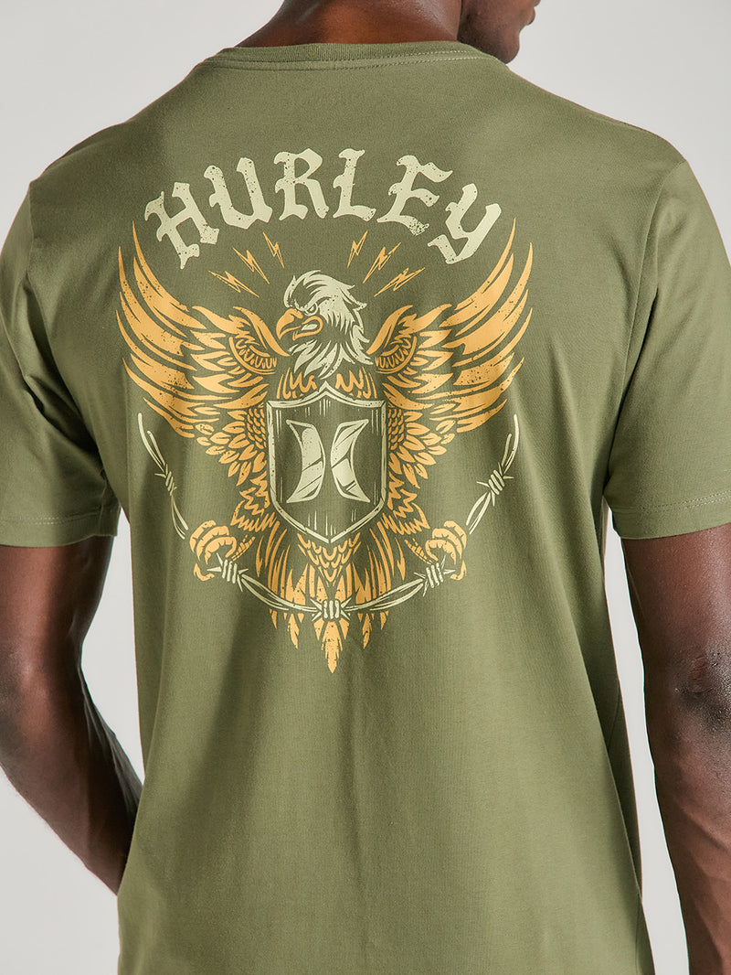 Camiseta verde militar manga curta estampa grande nas costas, apresentando uma águia dourada estilizada com asas abertas, escudo central e o texto "Hurley" acima.