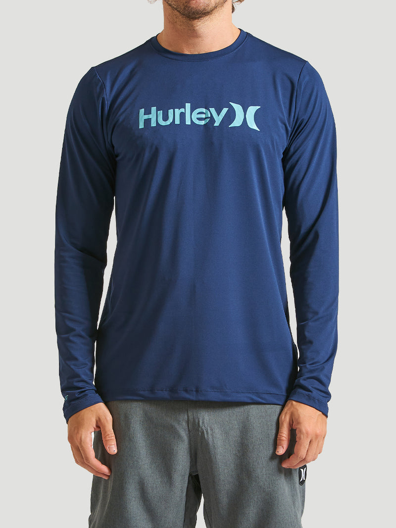Homem vestindo lycra surf manga longa azul marinho, com o logo Hurley azul claro no peito. Modelo ajustado, ideal para conforto e proteção solar.