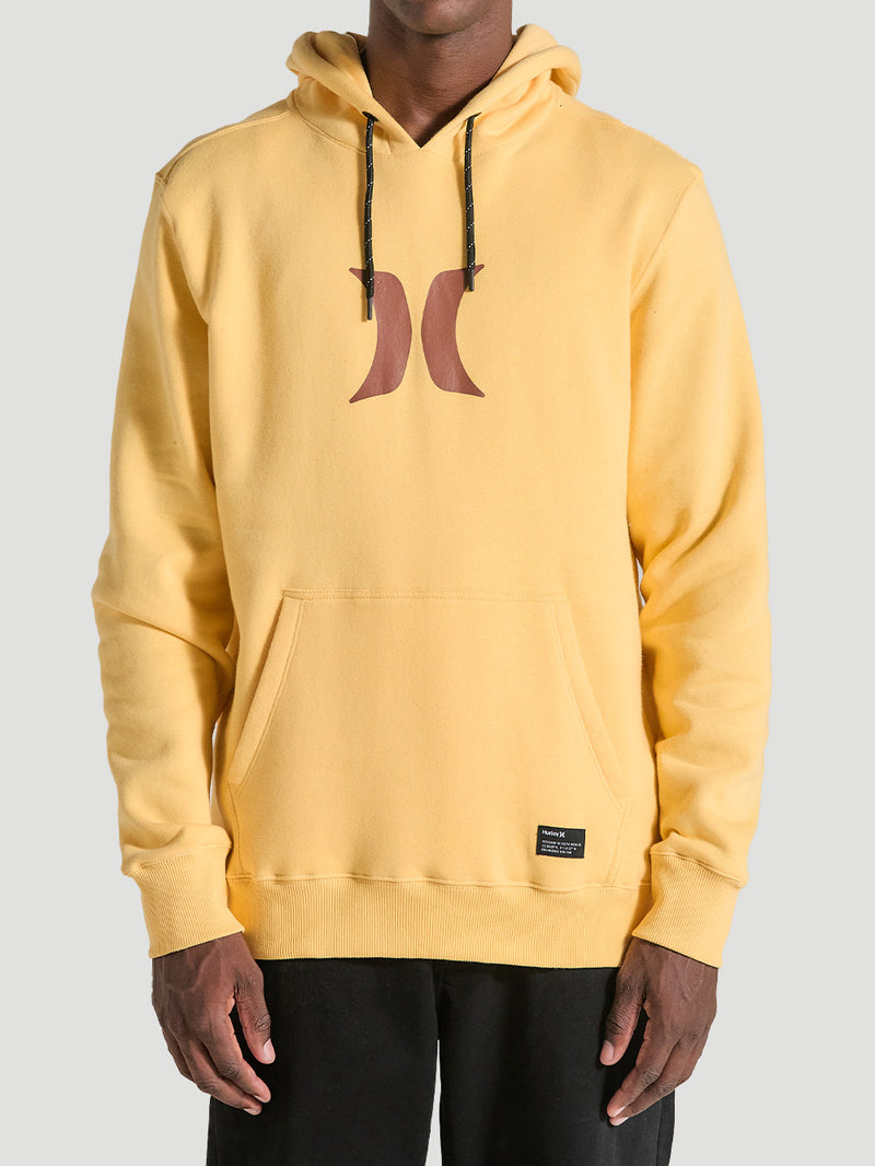 Homem vestindo um moletom canguru amarelo básico Hurley Icon, com capuz ajustável por cordões pretos, bolso frontal e logo marrom centralizado no peito.