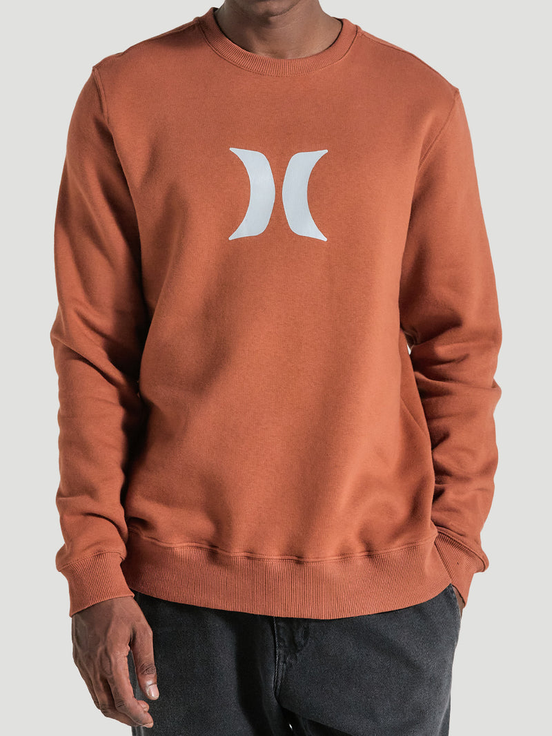 Pessoa vestindo moletom careca marrom com logo branco no centro, mangas longas, punhos e barra ajustados, combinado com calça preta.