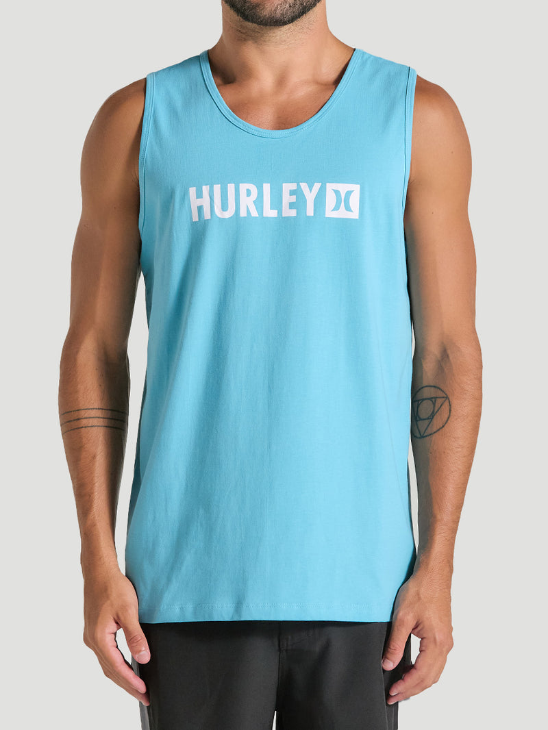 Homem vestindo regata azul casual com o logo "Hurley" em branco centralizado no peito. A peça tem corte reto, alças largas e tecido leve.
