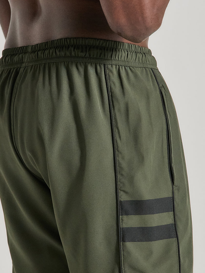 Close de shorts tactel verde militar 17 polegadas com cós elástico, detalhe de duas faixas pretas na lateral e recorte discreto no bolso lateral.