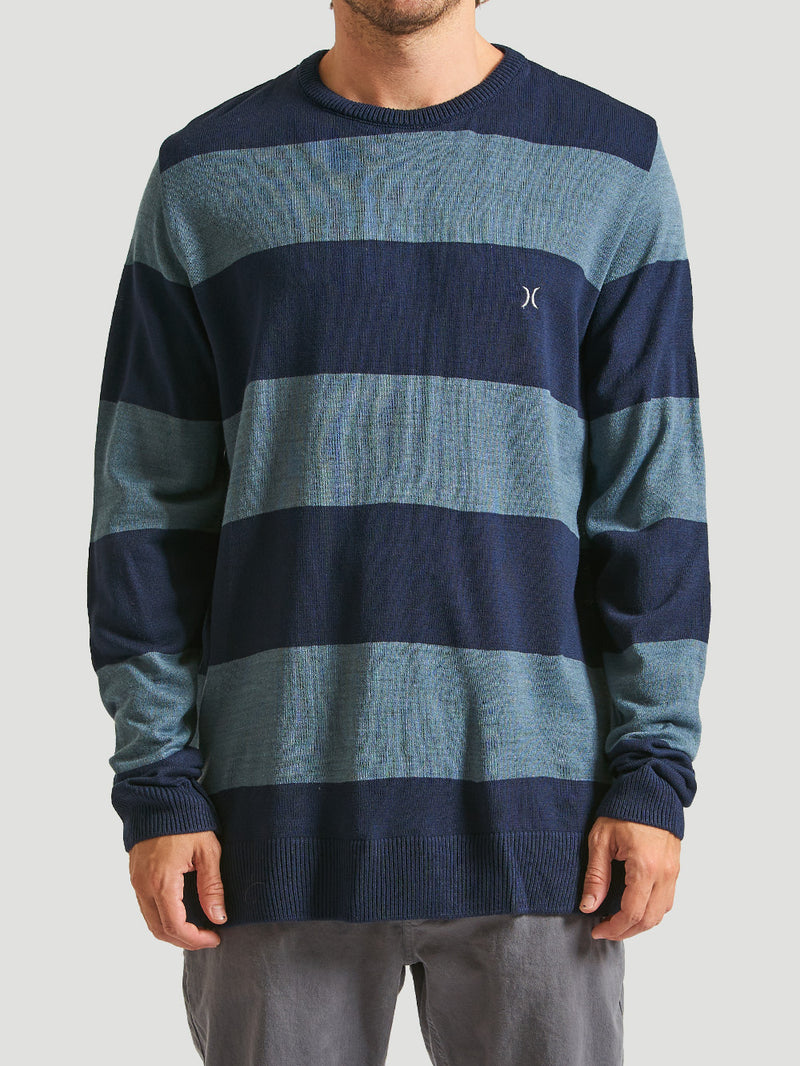 Homem vestindo um tricot listrado azul marinho com gola redonda e acabamento canelado nas mangas e barra.