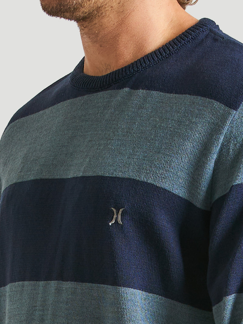 Close do tricot listrado azul marinho com detalhe de logo bordado no peito e gola redonda com acabamento canelado.