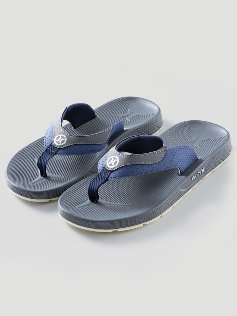 Chinelo branco Hurley e cinza com solado anatômico texturizado, tiras largas perfuradas e logotipo em destaque na parte superior. Design confortável e moderno.