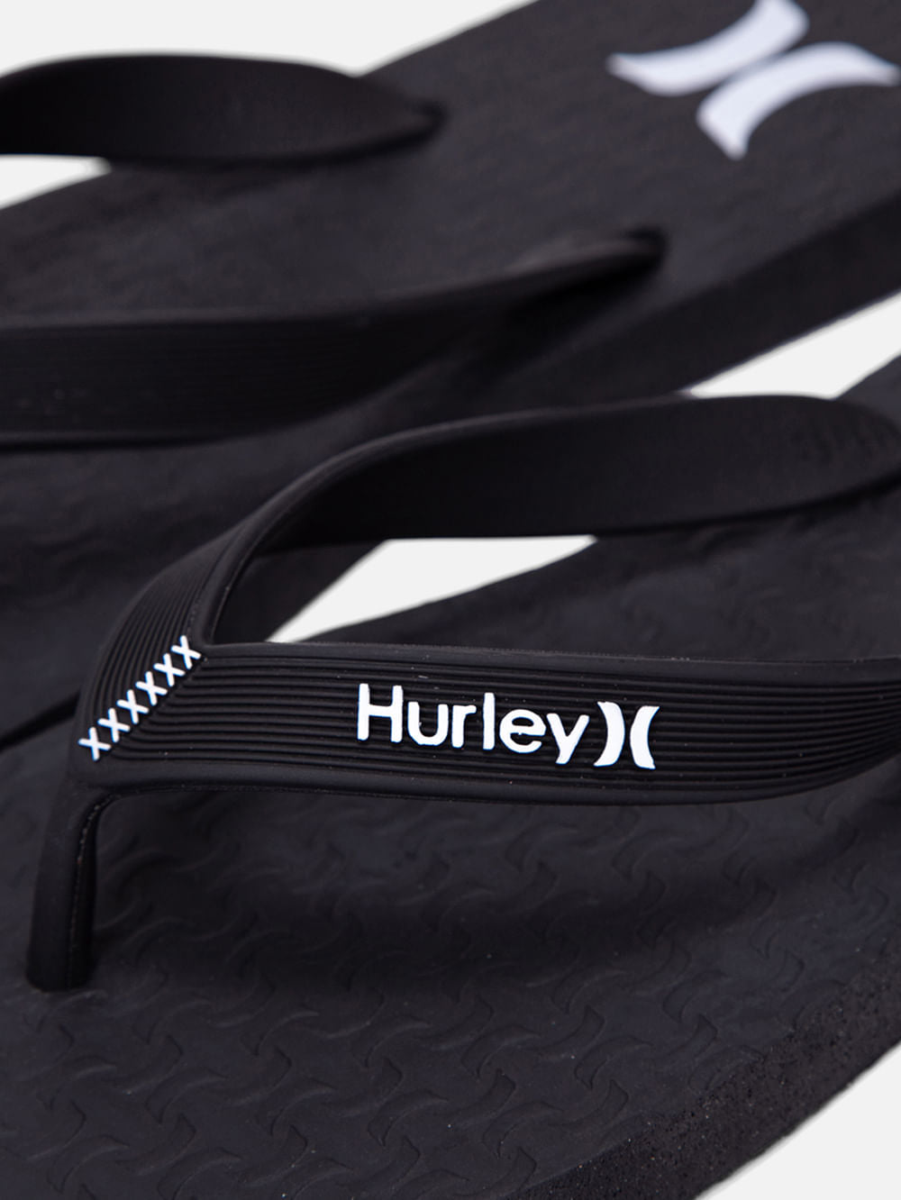 Chinelo Hurley preto com tiras emborrachadas, logotipo branco e detalhes texturizados no solado. Design casual e confortável.